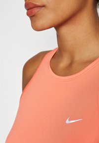 Top sportivo Nike in un vivace corallo, con design senza maniche. Presenta un collo a giro e il classico logo swoosh argentato sulla parte anteriore.