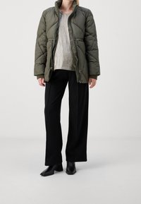 Oliwkowo-zielona pikowana kurtka z wzorem, pod spodem srebrny sweter o fakturze, zestawiona z czarnymi spodniami o szerokich nogawkach i botkami na obcasie.