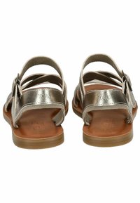 Sandali metallici argento con più cinturini, suola piatta color cuoio e dettaglio con fibbia. Il nome del marchio "TOMS" è visibile sul cinturino.