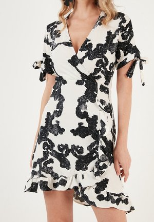 Robe portefeuille noire et blanche à manches courtes, ornée d'un motif floral, avec un ourlet à volants et des détails à nouer sur les manches. Tissu à texture lisse.