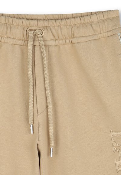 Pantalons de survêtement en coton beige avec une taille élastique, des détails de cordon de serrage et une poche latérale. Présente un logo cousu dans une teinte claire.