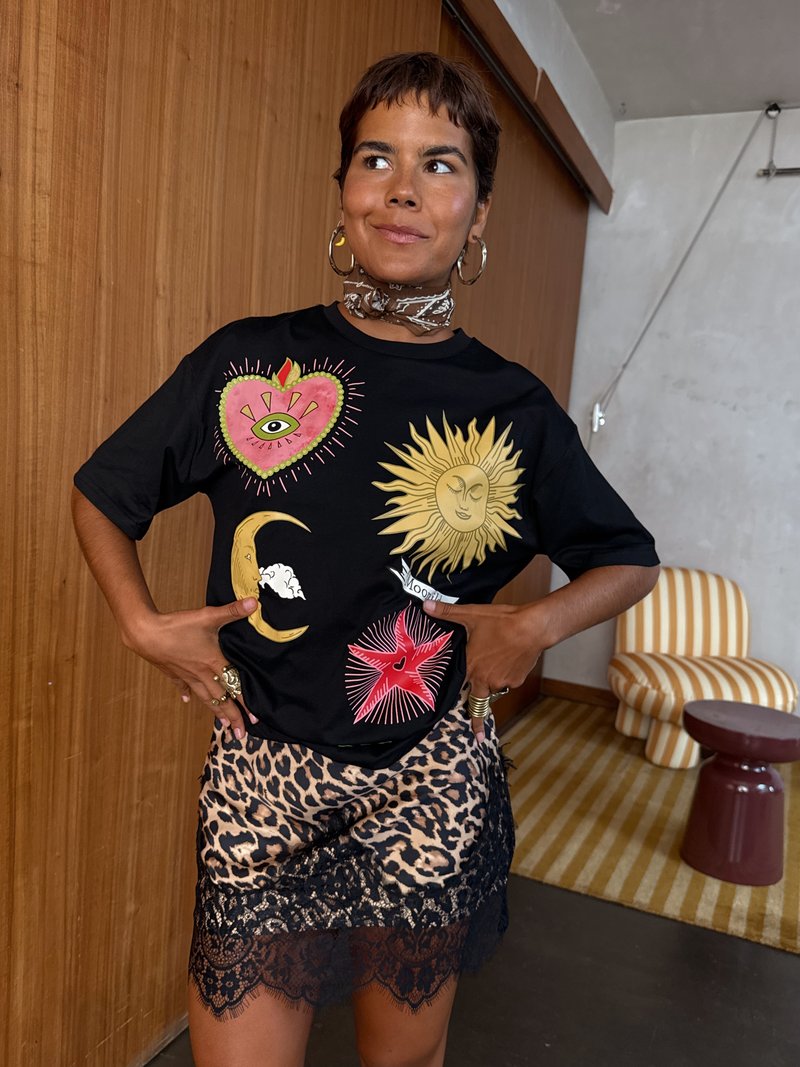 Tricou negru cu imprimeuri grafice colorate ale unei inimi, soarelui, lunii și stelei; asociat cu o fustă cu imprimeu leopard, având dantelă la margine.