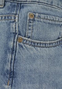Ljust blå denimtyg med en liten framficka med silvernitar och beige sömmar, som visar en blekt struktur.