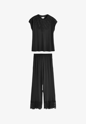 Crna kratka majica s detaljem čipke na izrezu uparen s odgovarajućim širokim hlačama s čipkastim obrubom na rubu.