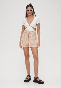 Wit cropped top met een centrale uitsnijding en korte mouwen, gecombineerd met meerkleurige gestreepte shorts met een riem in de taille en een relaxte pasvorm.