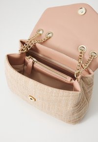 Beige textilhandväska med kviltad textur, guldkedjehandtag och en rosa läderinteriör. Innehåller en zip-pocket och tryckknapps-stängning.