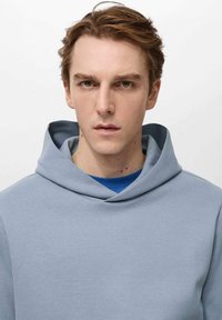 Light blue hooded sweatshirt with a smooth texture and wide neckline, layered over a dark blue shirt. Simple design with no patterns or accents.