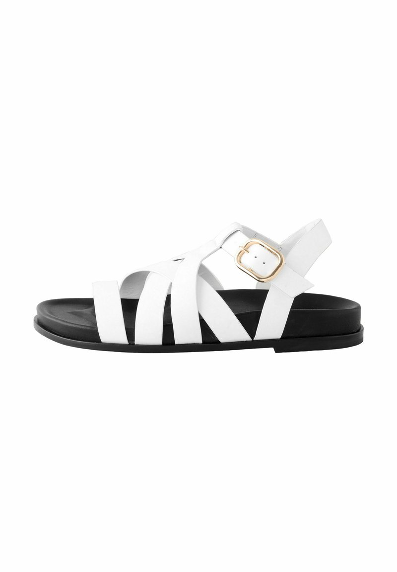 Sandales blanches à lanières avec une semelle noire et un détail en boucle en or. Elles présentent un design plat et un matériau lisse avec des lanières larges et superposées.