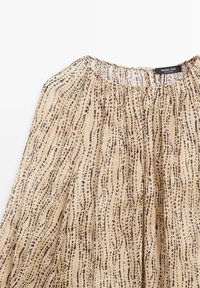 Beige Bluse mit Rundhalsausschnitt, die ein zartes, längliches gepunktetes Muster in Braun aufweist. Leichter Stoff mit gerafftem Design.