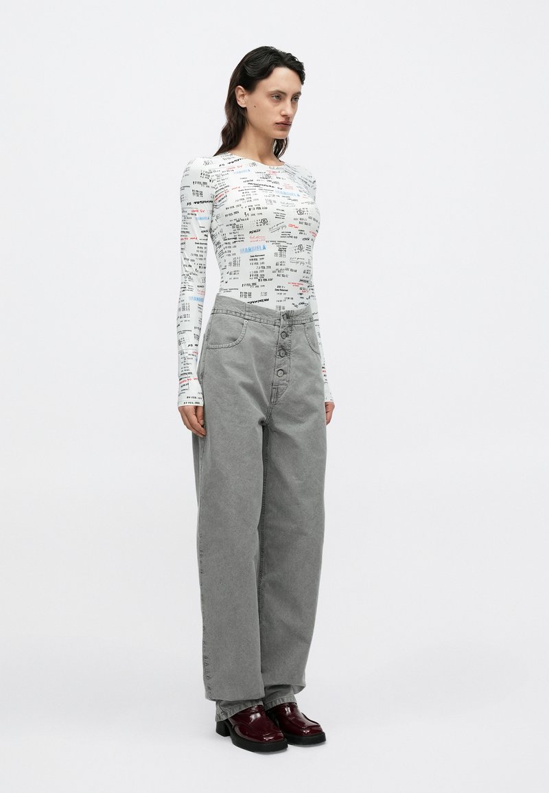 Langärmliges Hemd mit Grafikdruck in Weiß und Rot. Locker sitzende graue Hose mit hoher Taille und Fünf-Knopf-Verschluss. Glänzende Schuhe in dunklem Burgunderrot.