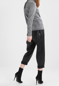 Svarta läderbyxor med uppvikta benslut, ihopparade med en grå rutigt långärmad topp. Modellen bär svarta högklackade ankelstövlar.