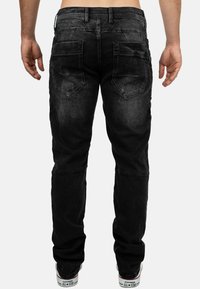 Jean en denim noir à coupe droite, cinq poches et coutures contrastées. Présente une texture légèrement décolorée et un détail de marque à l'arrière.