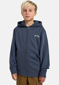 Granatowa bluza z kapturem na zamek, wykonana z miękkiego materiału, z przednią kieszenią i ściągaczami na rękawach. Logo marki na lewej stronie klatki piersiowej.