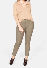 Top beige a maniche lunghe con colletto e scollo a V, abbinato a pantaloni aderenti marroni a motivo pied de poule e scarpe marroni scure con dettaglio fibbia.