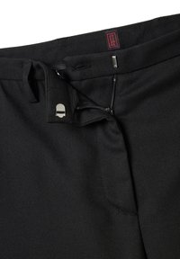 Zwarte stoffen broeken met een gestructureerde afwerking, voorzien van een ritssluiting aan de voorkant, een tailleband met strik en een rood label dat op de tailleband is gestikt.