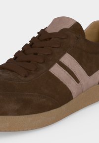 Baskets en daim marron avec des rayures rose clair sur le côté, des lacets marron et une semelle en caoutchouc beige.