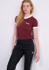 T-shirt bordeaux a maniche corte con bordi bianchi, con logo "Dickies". Abbinato a pantaloni della tuta neri, design a tre strisce bianche e cerniera laterale.