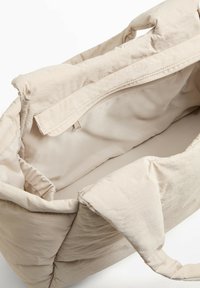 Borsa a spalla in tessuto morbido beige, con apertura ampia, dotata di tasca con zip e superficie testurizzata. Manici sulla parte superiore per un facile trasporto.