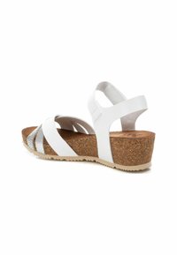 Sandalias blancas con suela de cuña de corcho, que presentan acentos plateados y múltiples tiras entrecruzadas. Textura suave y correa trasera ajustable.