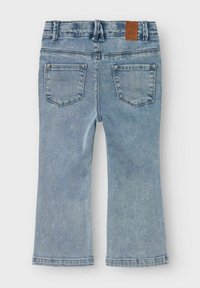 Jean flare en denim bleu clair, avec une taille haute, des poches arrière cousues et un patch en cuir marron à la taille. Texture lisse.