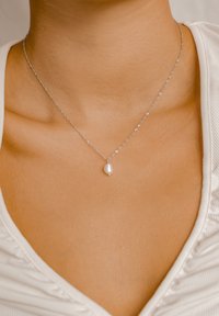 Collar de cadena de plata con un solo colgante de perla blanca de superficie suave y brillante, lucido sobre piel desnuda.