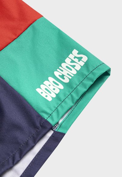 Close-up of color-blocked fabric with red, green, and navy sections, featuring white "BOBO CHOSES" text along the green panel.