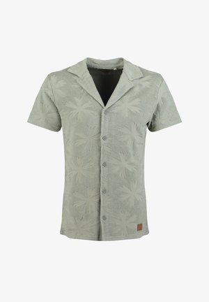 Camicia verde salvia a maniche corte con bottoni, motivo floreale in rilievo e colletto da campo, con una piccola toppa marrone vicino all'orlo inferiore.