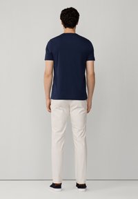 Granatowa koszulka z krótkim rękawem wykonana z gładkiego materiału, w zestawieniu z jasnobeżowymi, dopasowanymi spodniami i casualowymi ciemnymi sneakersami.