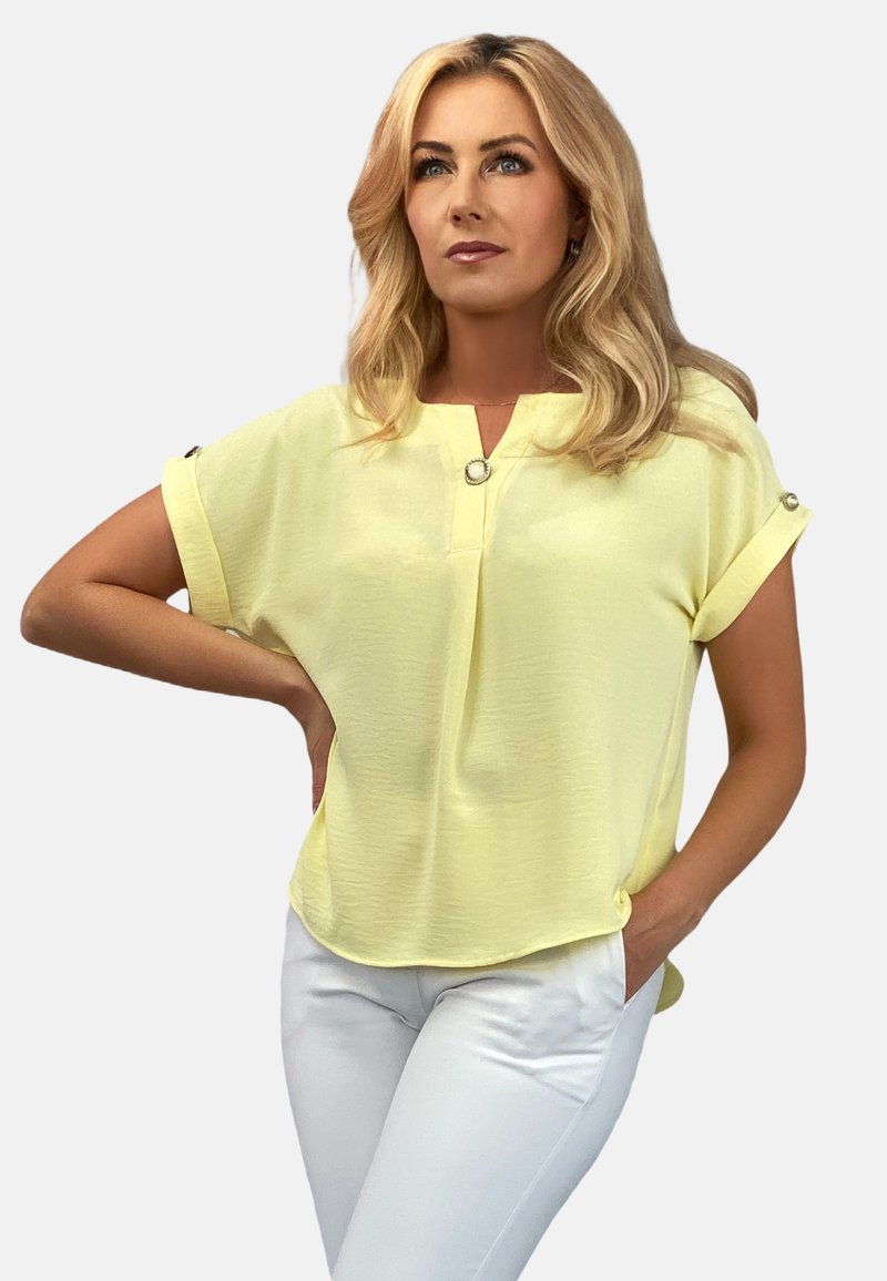 Żółta bluzka krótki rękaw z dekoltem w serek, z guzikiem na ramieniu, zestawiona z białymi spodniami. Miękki, lekki materiał.