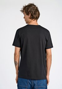 Sort bomulds t-shirt med rund halsudskæring, korte ærmer og en afslappet pasform, vist fra ryggen. Blå denimbukser synlige forneden.