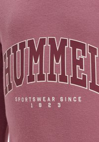 Bordeaux sweatshirt med stort hvidt "HUMMEL" bogstaver og mindre tekst "SPORTSWEAR SINCE 1923" nedenfor. Blød tekstur og afslappet design.