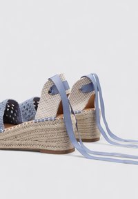 Sandalias de cuña con suela de yute trenzado, tiras de tela en azul claro y beige, con detalles en cinta y talones abiertos para mayor ajustabilidad.