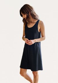 Vestido negro sin mangas, hecho de algodón suave, que presenta un corte relajado, escote redondo y longitud hasta mitad del muslo. Textura suave sin patrones.