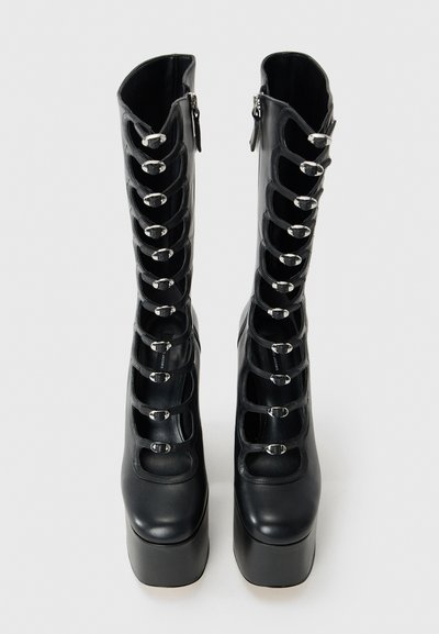 Bottes à plateforme noires avec de multiples découpes et des sangles à boucles argentées sur le devant, dotées de fermetures éclair sur le côté.