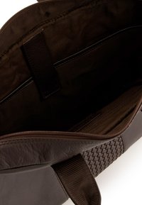 Brązowa skórzana torba tote z plecionymi akcentami, z zamknięciem na zamek błyskawiczny i ciemnym wnętrzem wykończonym kieszeniami do organizacji.