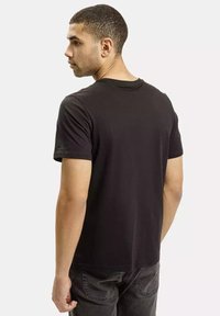 Czarna koszulka z krótkim rękawem wykonana z bawełny, z okrągłym dekoltem i gładką fakturą. Model pokazany z tyłu, bez widocznych grafik.