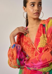 Rochie cu imprimeu floral colorat, cu maneci lungi tip puff, decolteu în V și talie strânsă. Fabricată dintr-un material ușor și transparent, cu nuanțe vibrante.