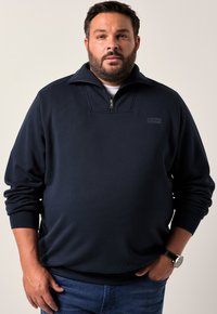 Felpa blu navy con mezza zip, colletto alto, maniche lunghe e un piccolo logo sul petto. Realizzata in un tessuto morbido.