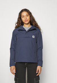 Marineblaues, leichtes Anorak mit einer Fronttasche, elastischen Bündchen und einer Kapuze. Hergestellt aus glattem, wasserabweisendem Material. Mit Logo-Patch.