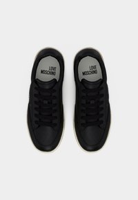 Ζευγάρι μαύρα sneakers Love Moschino με σχεδιασμό κορδονιών και λευκές σόλες, από πάνω σε λευκό φόντο.