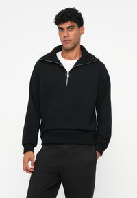 Zwarte sweatshirt met een hoge kraag en een half-rits ontwerp. Kenmerken ribgebreide manchetten en een zoom, gemaakt van een gladde, zware stof.