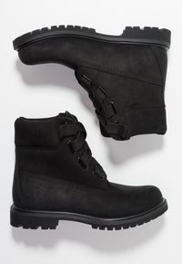 Black ankle boots made of rubber with a matte finish, featuring a lace-up design and a rugged tread sole for traction.