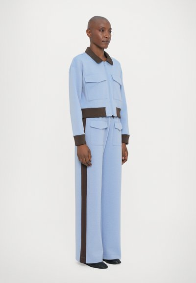 Lyseblå cropped jakke med brun krage og mansjetter, med to brystlommer, sammen med matchende vide bukser med en brun stripe.