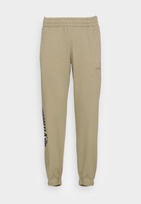 Gaišbrūnas sporta bikses ar elastīgu jostu un aprocēm. Satur sānu kabatas un drukātu tekstu uz kreisās kājas. Mīksta, gluda tekstūra.