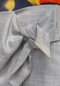Tejido gris con un acabado texturizado, que presenta un detalle de nudo. El tejido tiene un sutil patrón de cuadros, que enfatiza su diseño tejido.