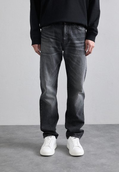 Schwarze Kapuzenjacke kombiniert mit grauen Denim-Jeans. Die Jeans haben ein verwaschenes Design, einen geraden Schnitt und werden mit weißen Sneakern getragen.