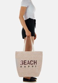 Große Tragetasche mit beigem gewebtem Muster und weißem Zickzackmuster. Verziert mit Pailletten-Schriftzug "BEACH HAPPY" in dunkelbraun. Integrierte Griffe.