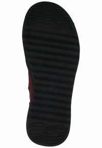 Suela de zapato de goma negra con un patrón de agarre texturizado y líneas curvas, que presenta un logotipo elevado en el centro y bordes suaves.