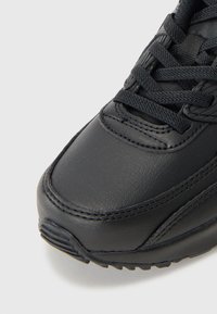 Baskets en cuir noir avec coutures détaillées, surface texturée et design à lacets. Équipées d'une semelle en caoutchouc et d'une capuchon renforcé.