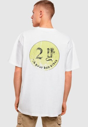 Hvid bomulds t-shirt med et rundt gult grafik med sort tekst og et slidt look. Løs pasform med korte ærmer og lige kant.